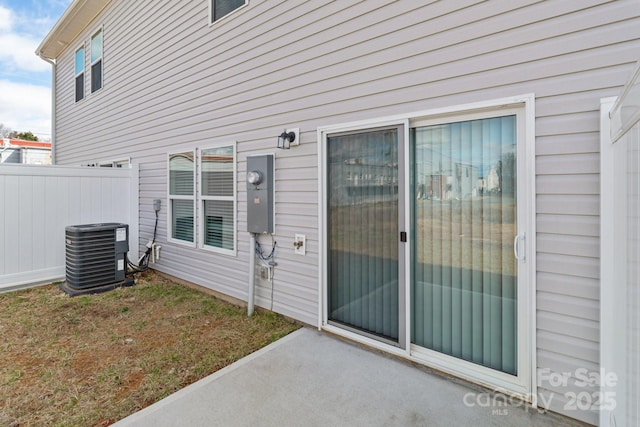 view of exterior entry featuring central AC and fence