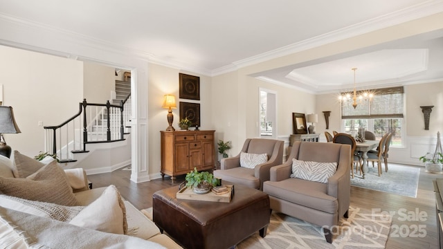 living room with stairway, an inviting chandelier, wood finished floors, and ornamental molding