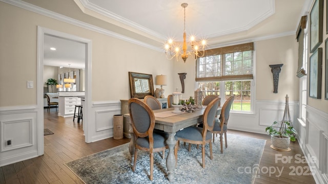 dining room featuring a chandelier, a raised ceiling, dark wood-type flooring, and ornamental molding