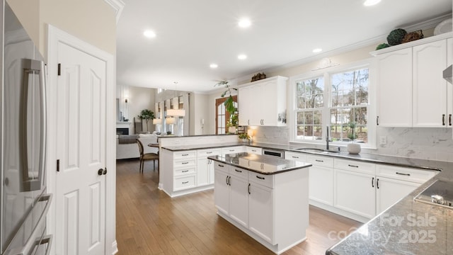 kitchen with backsplash, hardwood / wood-style floors, a peninsula, stainless steel fridge, and a sink