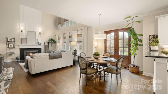 dining area with a glass covered fireplace, dark wood-style floors, french doors, and ornamental molding