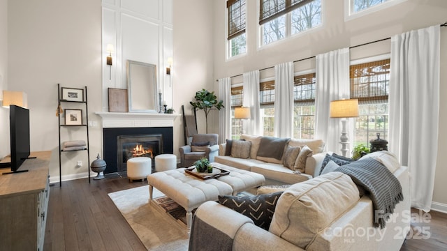 living room featuring a fireplace with flush hearth, a healthy amount of sunlight, dark wood-type flooring, and baseboards