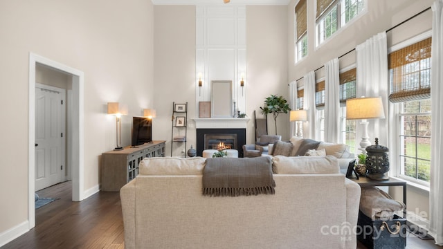 living area with dark wood finished floors, a glass covered fireplace, a high ceiling, and baseboards