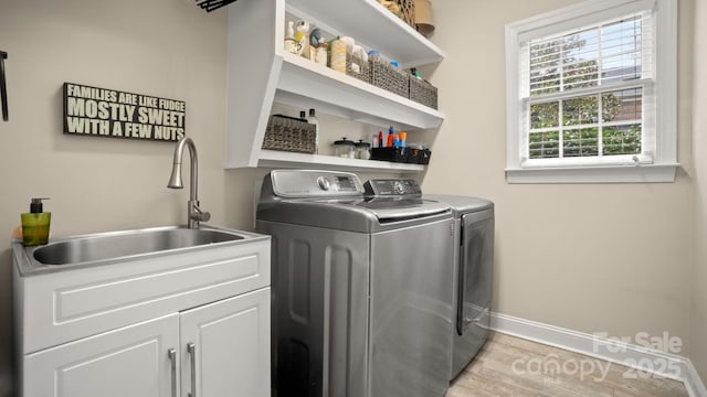 clothes washing area with baseboards, light wood finished floors, washing machine and clothes dryer, cabinet space, and a sink