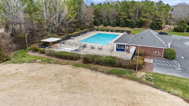 pool with a patio area, a wooded view, and fence