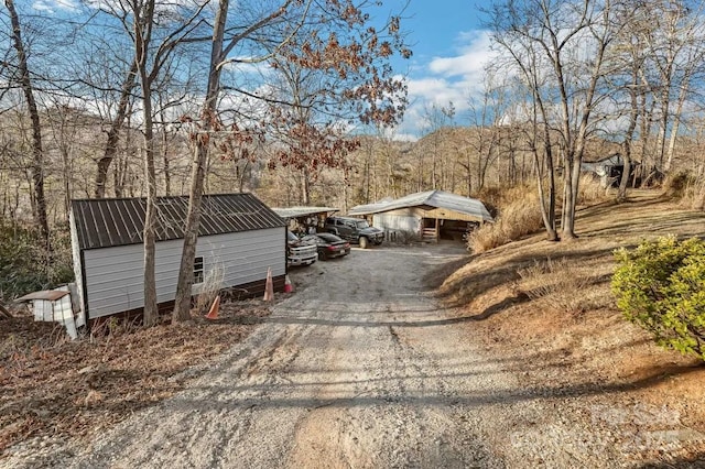 view of front facade featuring dirt driveway, metal roof, an outdoor structure, and a detached carport