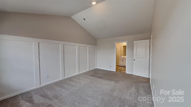 unfurnished bedroom with connected bathroom, multiple closets, vaulted ceiling, carpet flooring, and a decorative wall