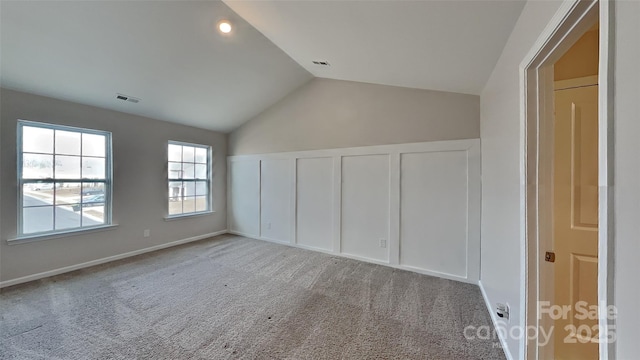 interior space with visible vents, carpet flooring, a decorative wall, and vaulted ceiling