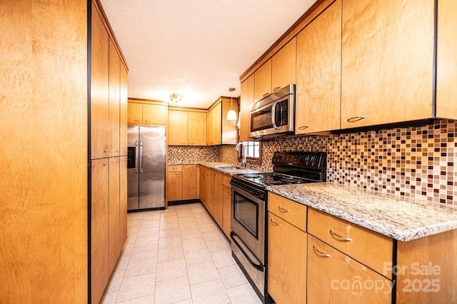 kitchen with stainless steel appliances, a sink, decorative backsplash, and light stone countertops