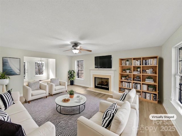 living room featuring a fireplace, a textured ceiling, wood finished floors, baseboards, and ceiling fan with notable chandelier