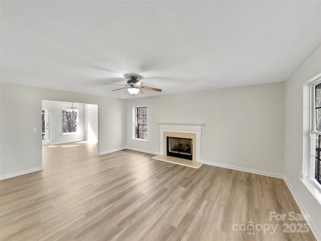 unfurnished living room with a fireplace, light wood-style flooring, baseboards, and ceiling fan with notable chandelier