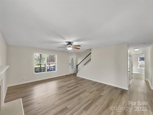 unfurnished living room with light wood-style floors, ceiling fan, stairway, and baseboards