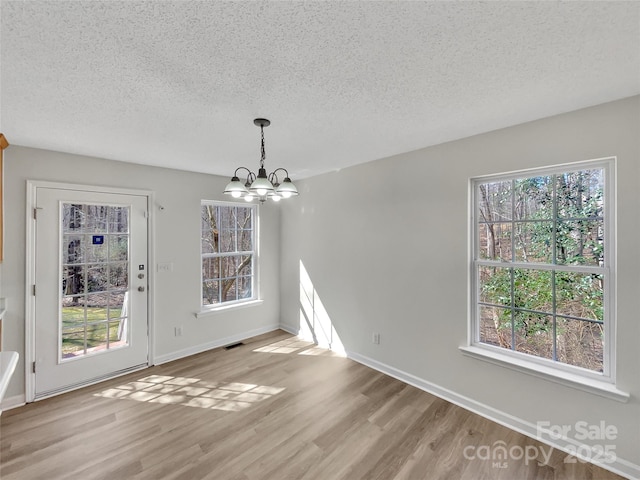 unfurnished dining area with a textured ceiling, light wood-type flooring, visible vents, and an inviting chandelier