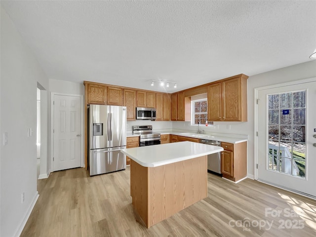 kitchen with a textured ceiling, stainless steel appliances, a sink, light wood-style floors, and light countertops