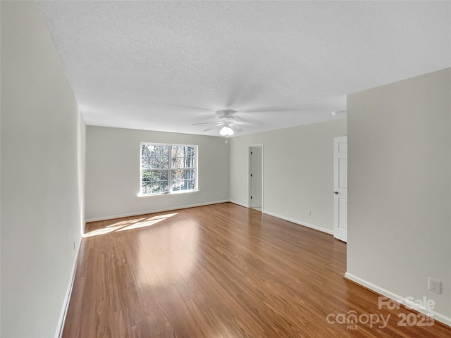 spare room with a textured ceiling, ceiling fan, wood finished floors, and baseboards