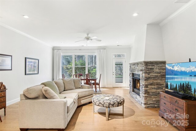 living room featuring a ceiling fan, crown molding, a stone fireplace, and light wood-style flooring