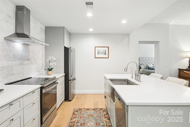 kitchen with a sink, stainless steel appliances, light wood finished floors, wall chimney exhaust hood, and visible vents