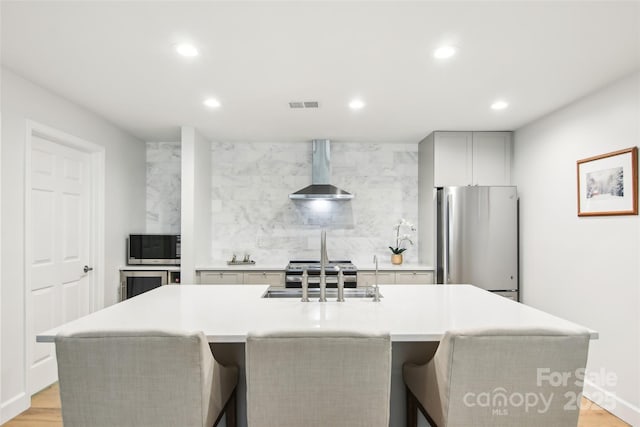 kitchen with a sink, stainless steel appliances, backsplash, wall chimney exhaust hood, and recessed lighting
