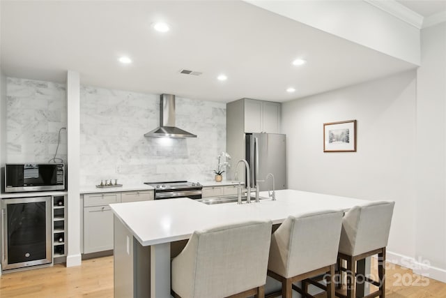 kitchen with tasteful backsplash, wall chimney exhaust hood, appliances with stainless steel finishes, wine cooler, and visible vents