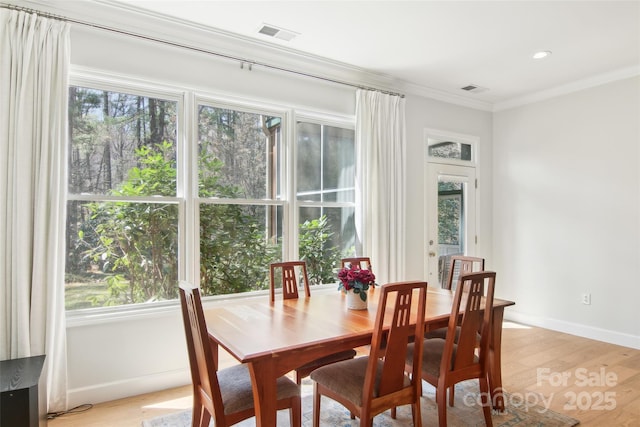 dining room featuring baseboards, light wood-style flooring, visible vents, and crown molding
