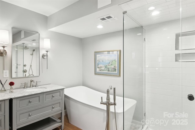 full bath featuring a freestanding bath, wood finished floors, visible vents, vanity, and a stall shower