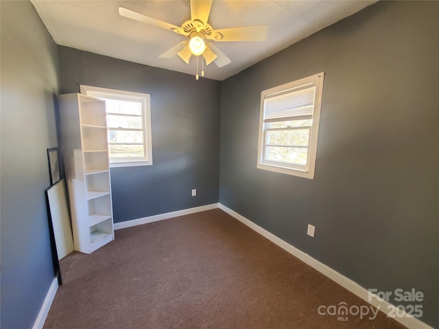 empty room with a ceiling fan, baseboards, and dark colored carpet