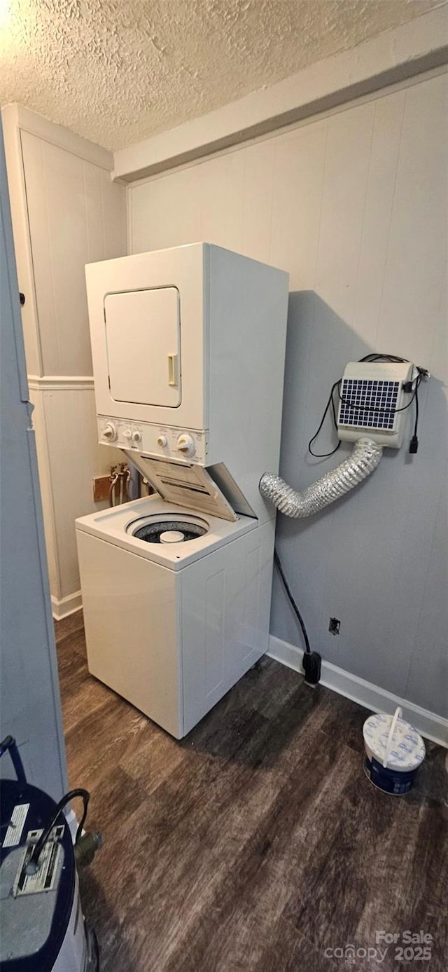 laundry room with a textured ceiling, dark wood-type flooring, stacked washer and dryer, and laundry area