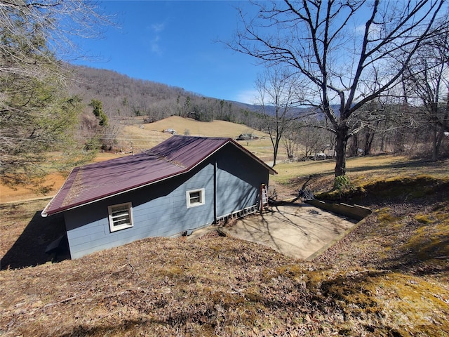 view of side of home featuring metal roof and a view of trees