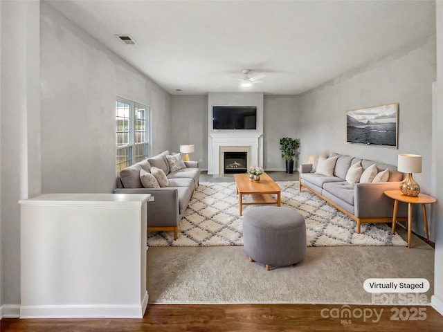 living room with a ceiling fan, visible vents, wood finished floors, and a glass covered fireplace