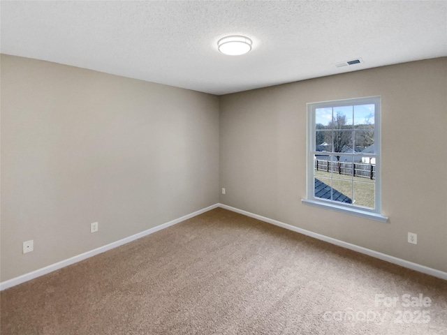 empty room with carpet flooring, visible vents, a textured ceiling, and baseboards