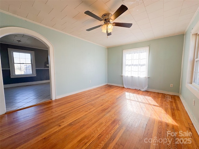 spare room with ornamental molding, arched walkways, baseboards, and hardwood / wood-style floors