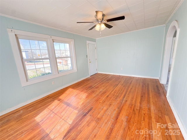 unfurnished room with arched walkways, a ceiling fan, baseboards, ornamental molding, and light wood finished floors