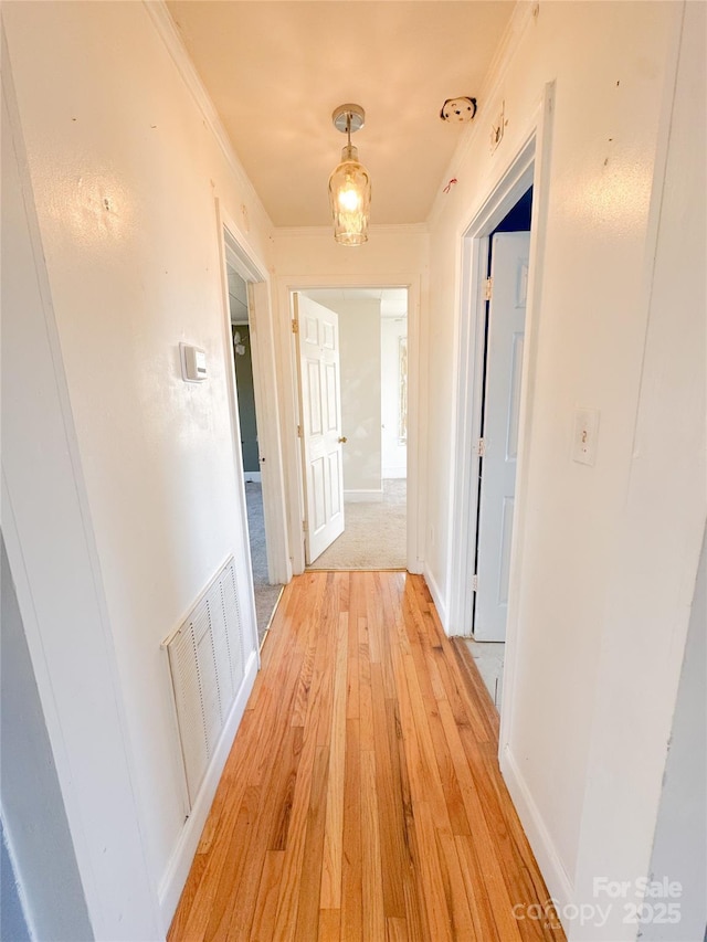 hall featuring baseboards, visible vents, crown molding, and light wood finished floors