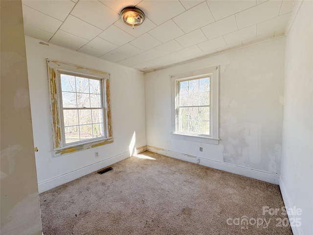 empty room with a wealth of natural light, baseboards, visible vents, and carpet