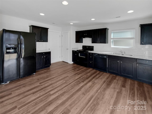 kitchen featuring light countertops, decorative backsplash, a sink, wood finished floors, and black appliances