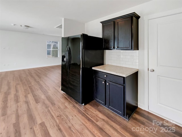 kitchen featuring tasteful backsplash, light wood-style flooring, open floor plan, light countertops, and black fridge