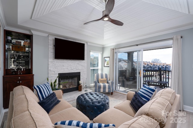 living room featuring a fireplace, wood finished floors, a ceiling fan, a raised ceiling, and crown molding