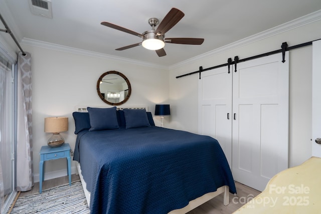 bedroom featuring ornamental molding, a barn door, wood finished floors, and visible vents