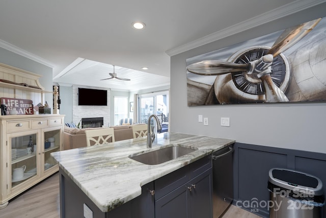 kitchen with dishwashing machine, a fireplace, a sink, ornamental molding, and light stone countertops