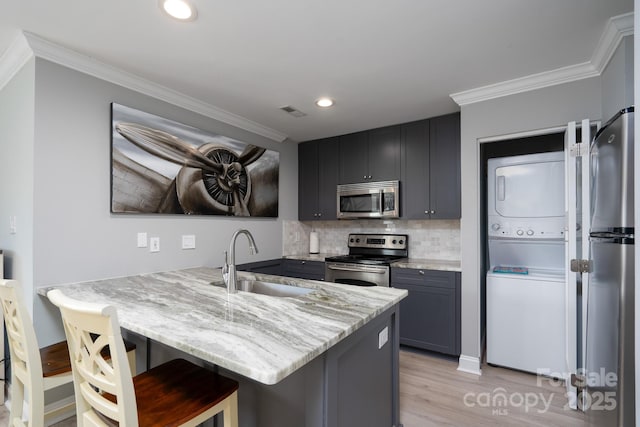 kitchen with a peninsula, a sink, ornamental molding, appliances with stainless steel finishes, and stacked washer and clothes dryer