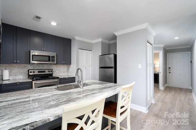 kitchen with light stone counters, a breakfast bar area, stainless steel appliances, a sink, and visible vents