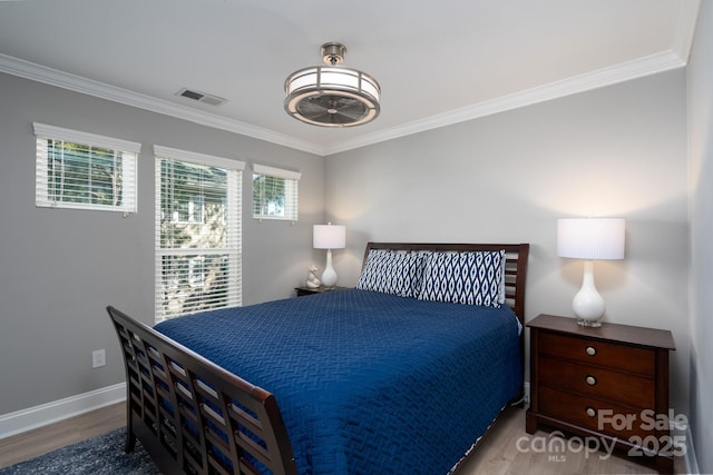 bedroom featuring baseboards, visible vents, crown molding, and wood finished floors