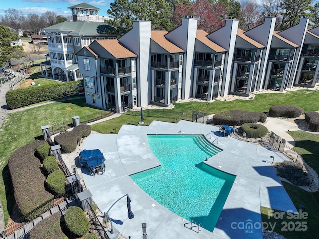 community pool featuring a patio, a lawn, fence, and a residential view