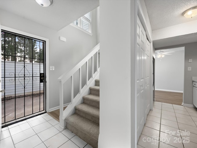 foyer featuring light tile patterned floors, a textured ceiling, a ceiling fan, baseboards, and stairway