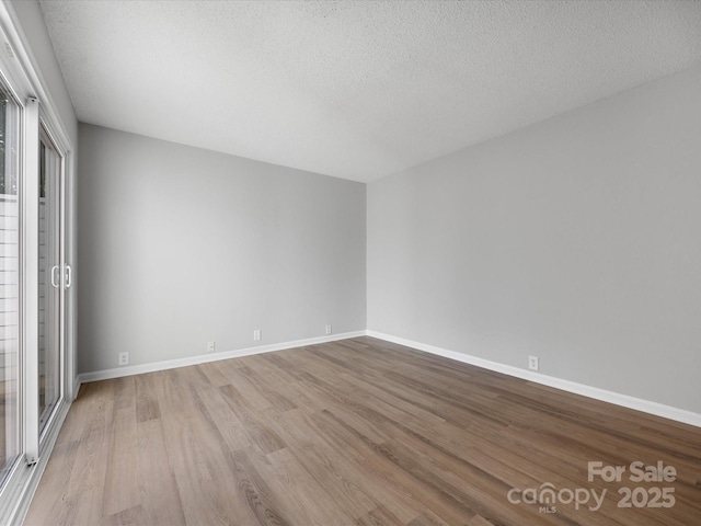 empty room featuring a textured ceiling, baseboards, and wood finished floors