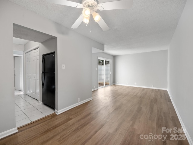 empty room featuring light wood-style floors, ceiling fan, a textured ceiling, and baseboards