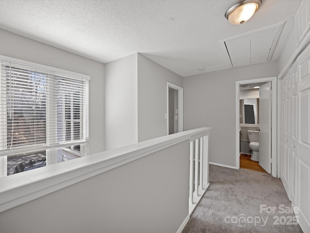 hall featuring a textured ceiling, light carpet, an upstairs landing, baseboards, and attic access