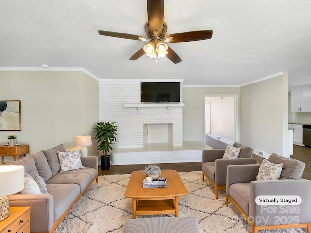 living room featuring a brick fireplace, a ceiling fan, crown molding, and wood finished floors