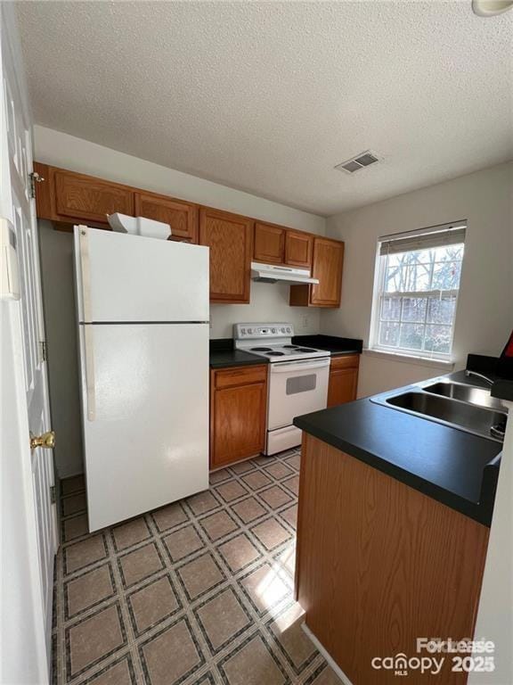 kitchen with dark countertops, light floors, brown cabinets, white appliances, and a sink