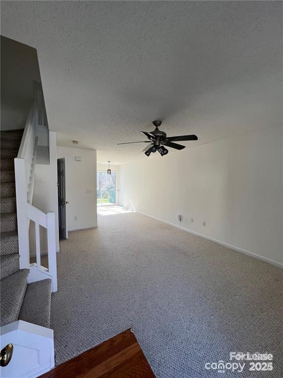 unfurnished living room with a textured ceiling, stairway, carpet floors, baseboards, and ceiling fan